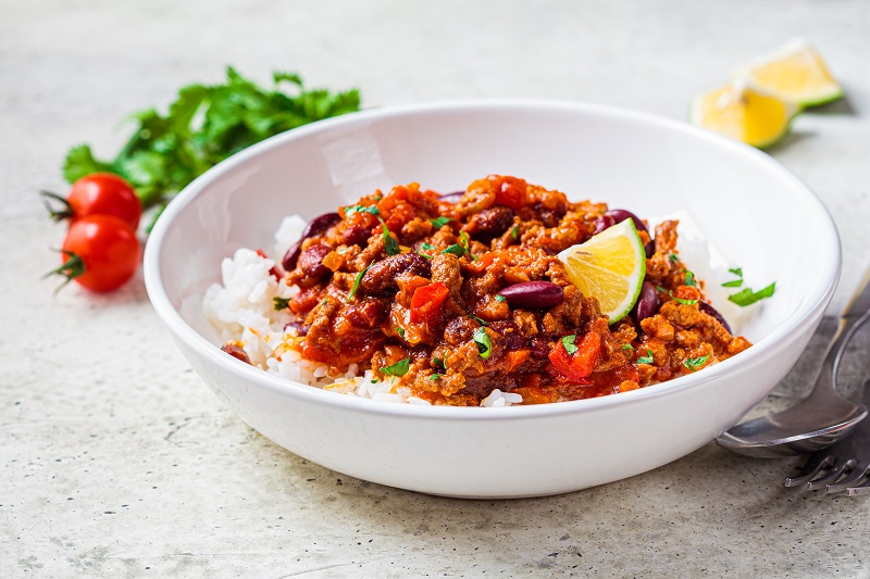 Chili con carne with rice in white bowl. Beef stew with beans in